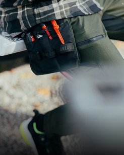 Person wearing a black tactical pouch with visible branding on a blurred background