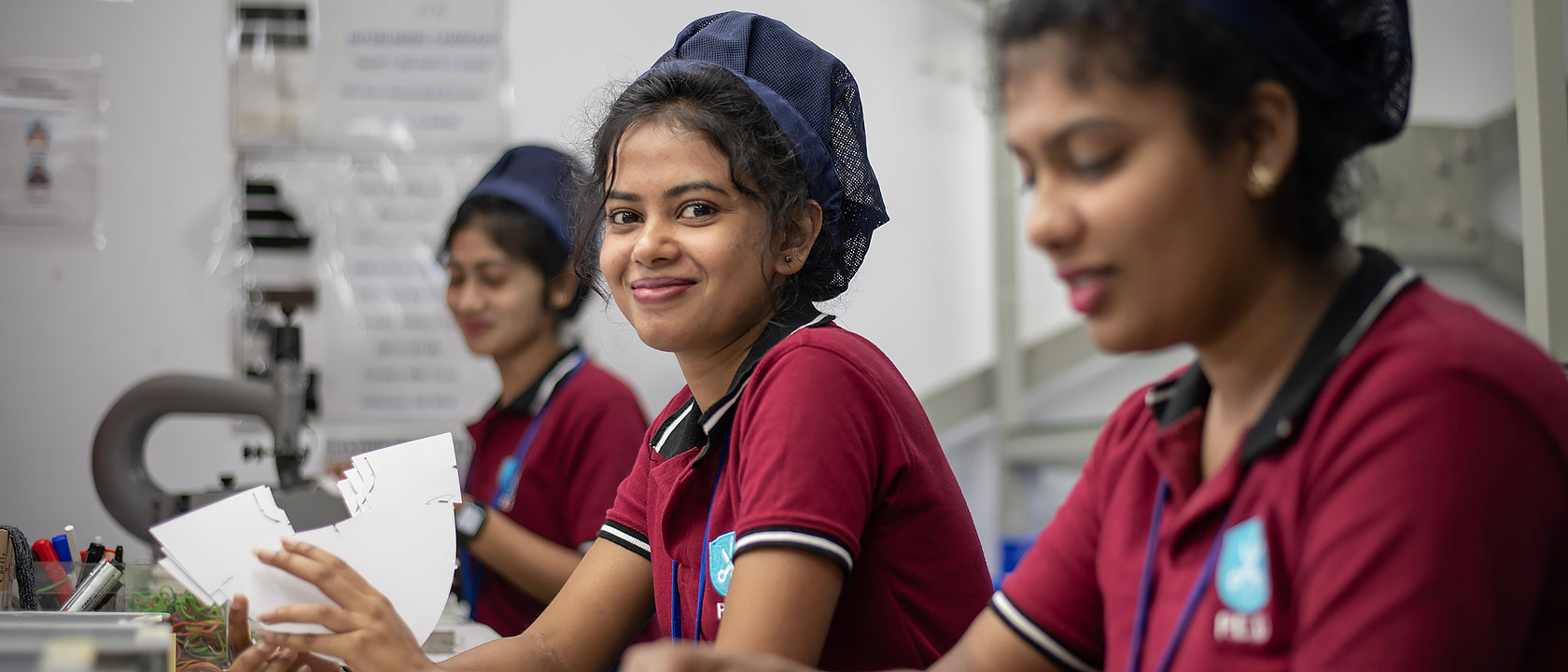 Two women in maroon uniforms with blue caps working in a factory setting.