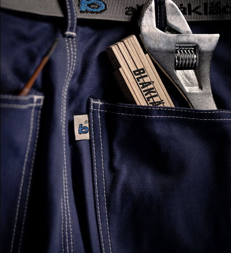Navy blue work pants with a wrench and pliers in the pocket, featuring 'BLÅKLÄDER' branding.