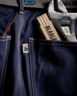 Navy blue work pants with a wrench and pliers in the pocket, featuring 'BLÅKLÄDER' branding.