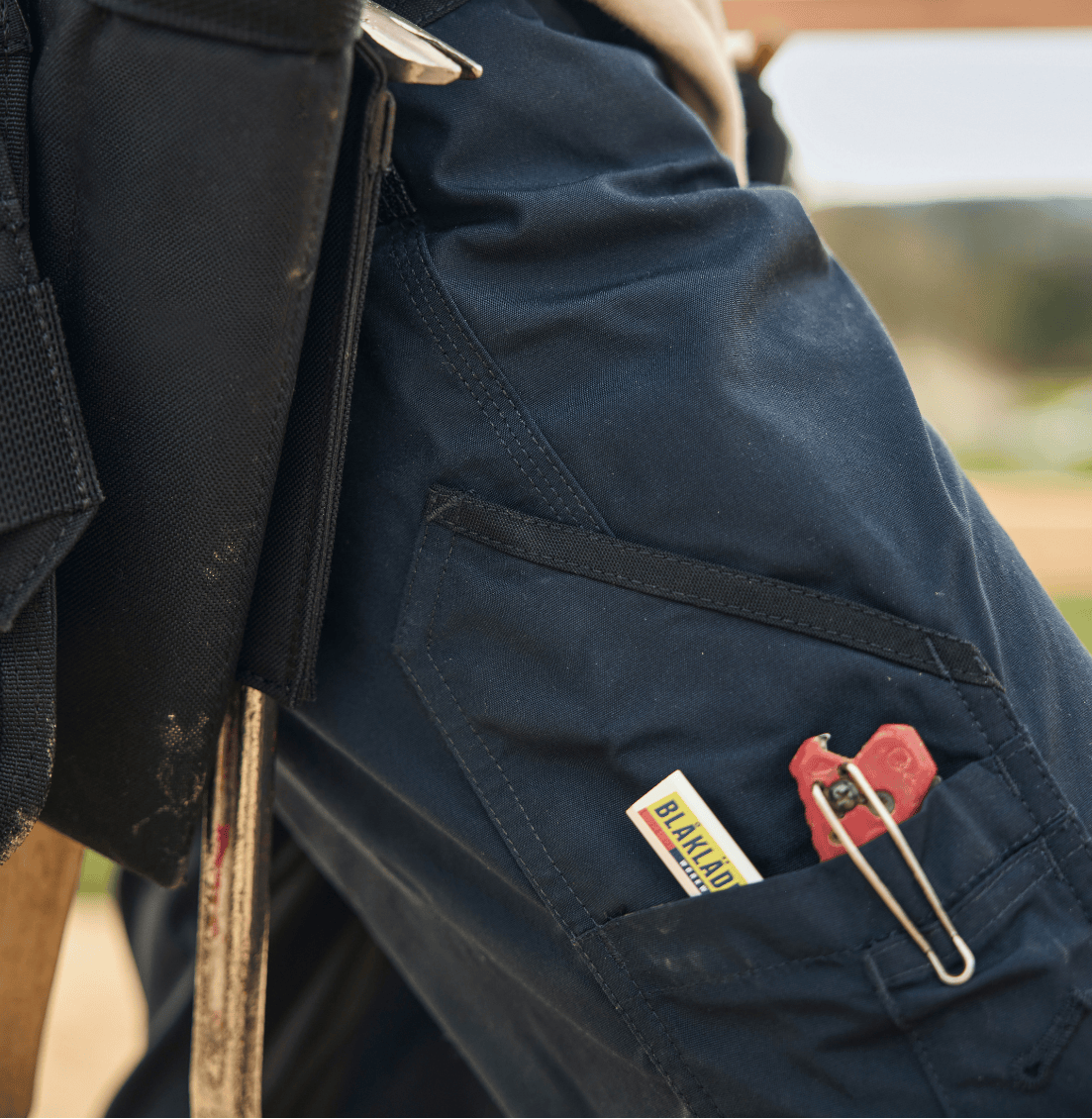 Person wearing navy blue work pants with tools and equipment, outdoors.