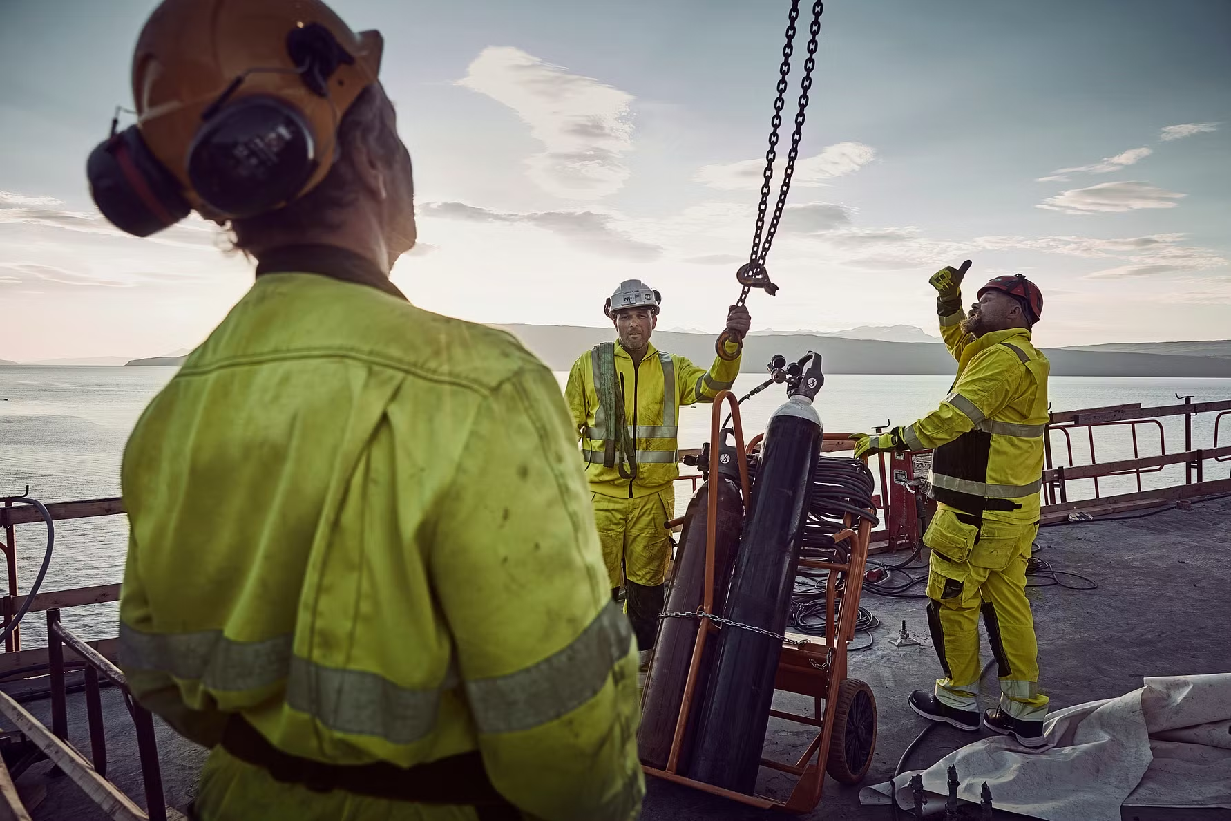 Workers in high-visibility clothing on a ship with equipment and ocean in the background