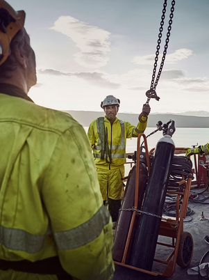 Workers in high-visibility clothing on a ship with equipment and ocean in the background