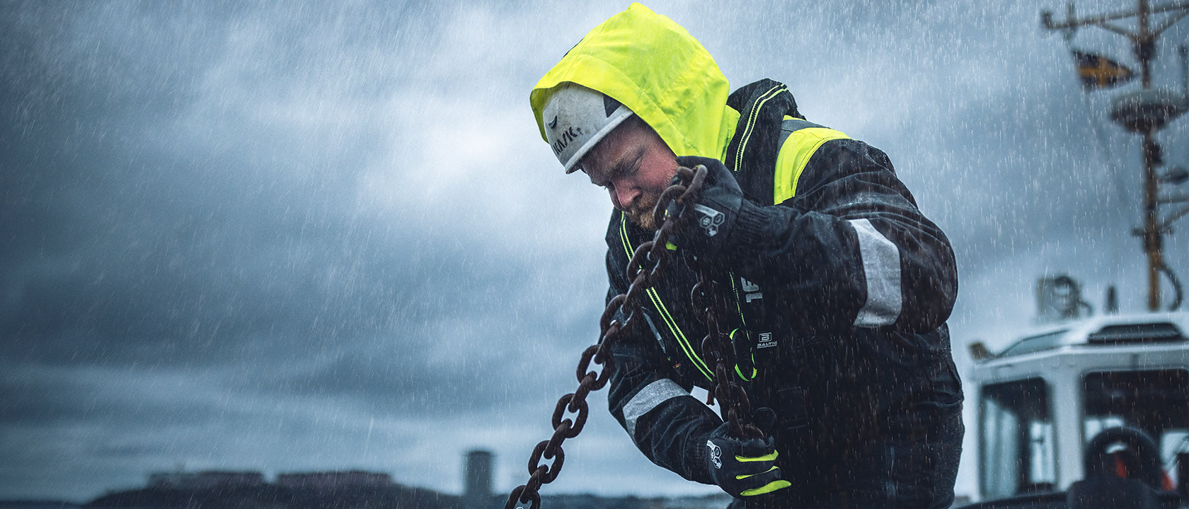 Person in a yellow raincoat and helmet holding a chain against a stormy background