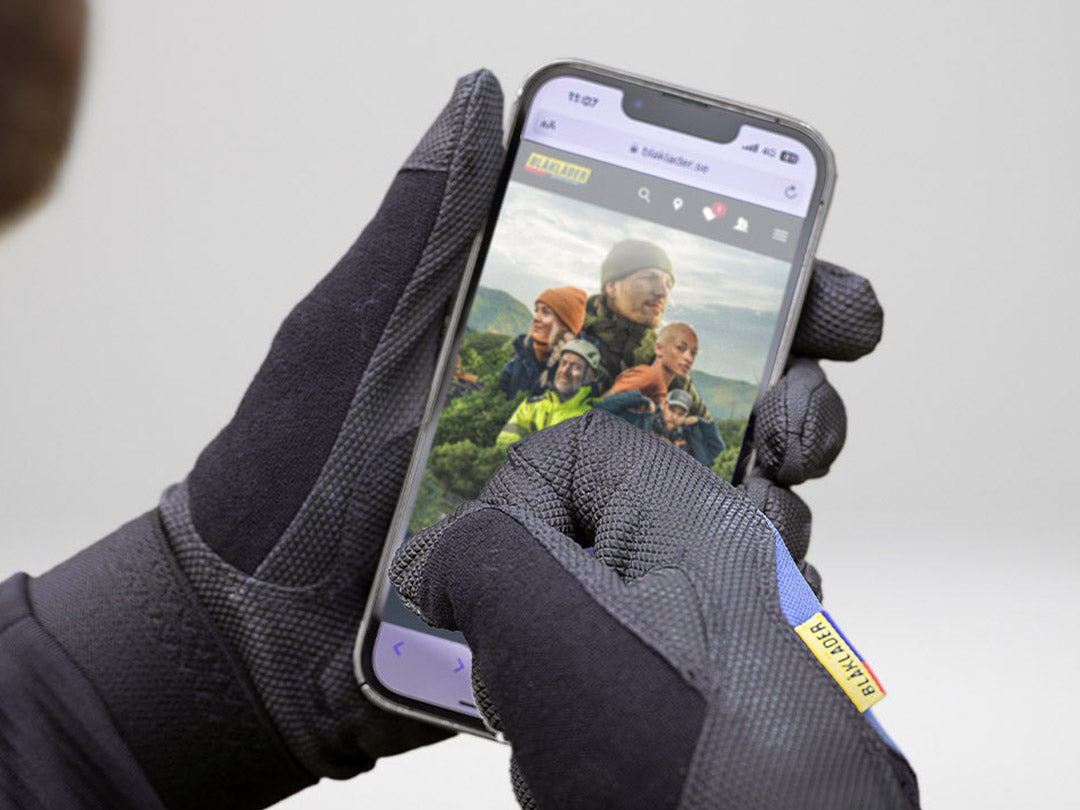 Person wearing gloves holding a smartphone with a screen displaying an image of people in outdoor clothing.